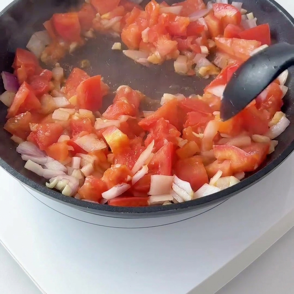 Gewürfelte Tomaten und rote Zwiebeln werden in einer Pfanne angedünstet, Tomatenmark wird untergerührt.