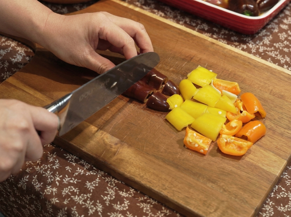 Paprika und Zwiebeln werden auf einem Holzbrett in kleine Stücke geschnitten.