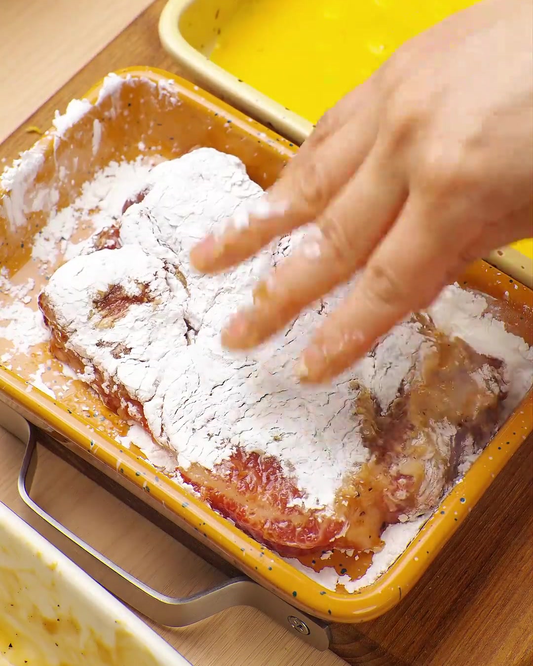 Eine Hand drückt ein in Ei gewendetes Schweinekotelett in eine Schale mit Panko-Paniermehl, um es vollständig zu ummanteln.