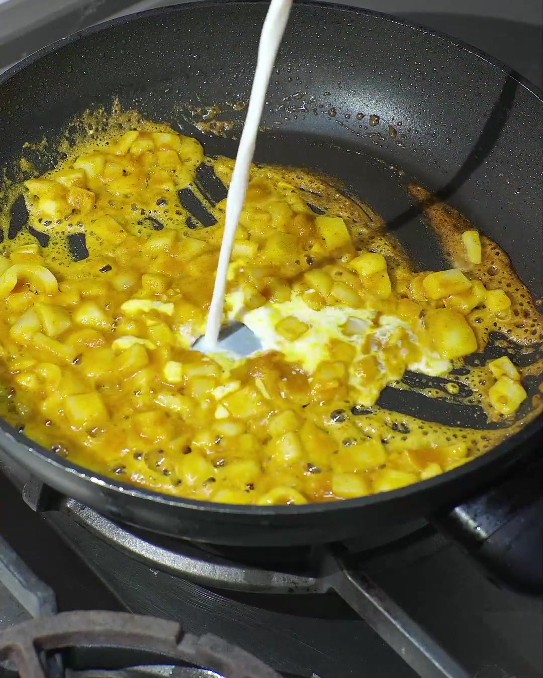 Kokosmilch wird in eine Pfanne mit geschmolzenem Curry und sautierten Zwiebeln gegossen, wodurch eine cremige gelbe Sauce entsteht.