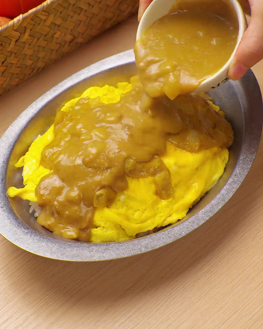 Eine reichhaltige, gelbe Currysauce wird aus einer kleinen Schüssel über ein Bett aus Rührei und Reis gegossen.