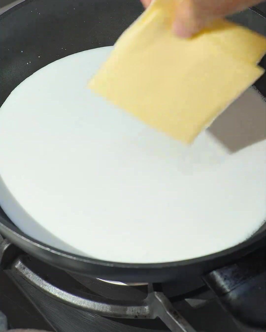 Zwei Scheiben gelber Käse schmelzen in köchelnder weißer Kokosmilch in einer dunklen Pfanne.