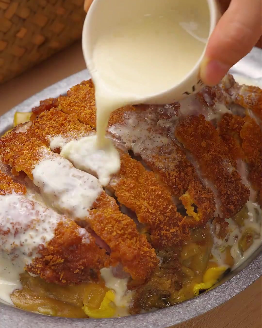 Eine Nahaufnahme einer cremigen weißen Käse-Kokos-Sauce, die über goldbraune, geschnittene Schweinekoteletts gegossen und mit frischer grüner Petersilie garniert wird.