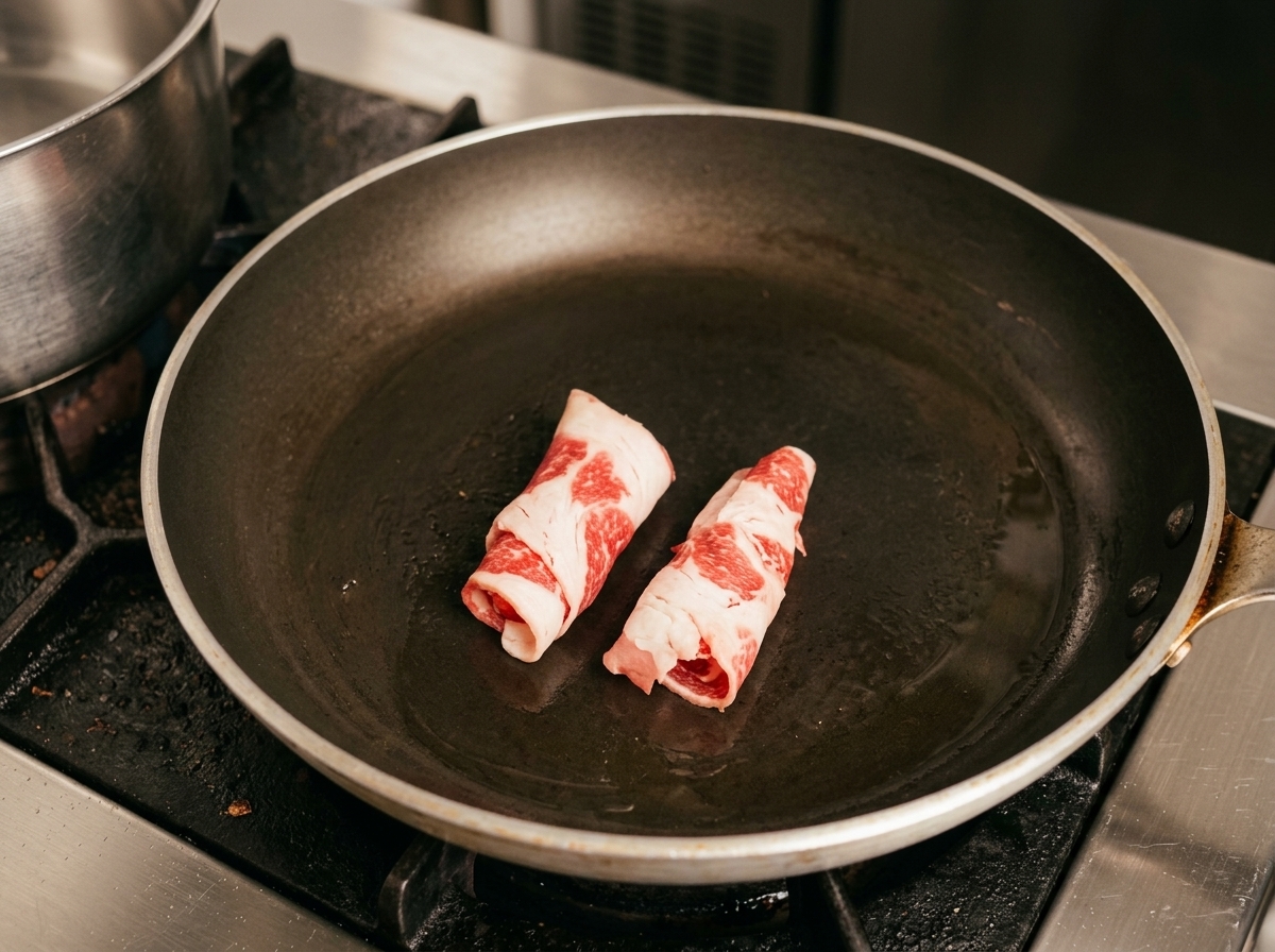 Gerollte Scheiben von rohem, fettreichem Rindfleisch werden in der heißen Pfanne gebraten.