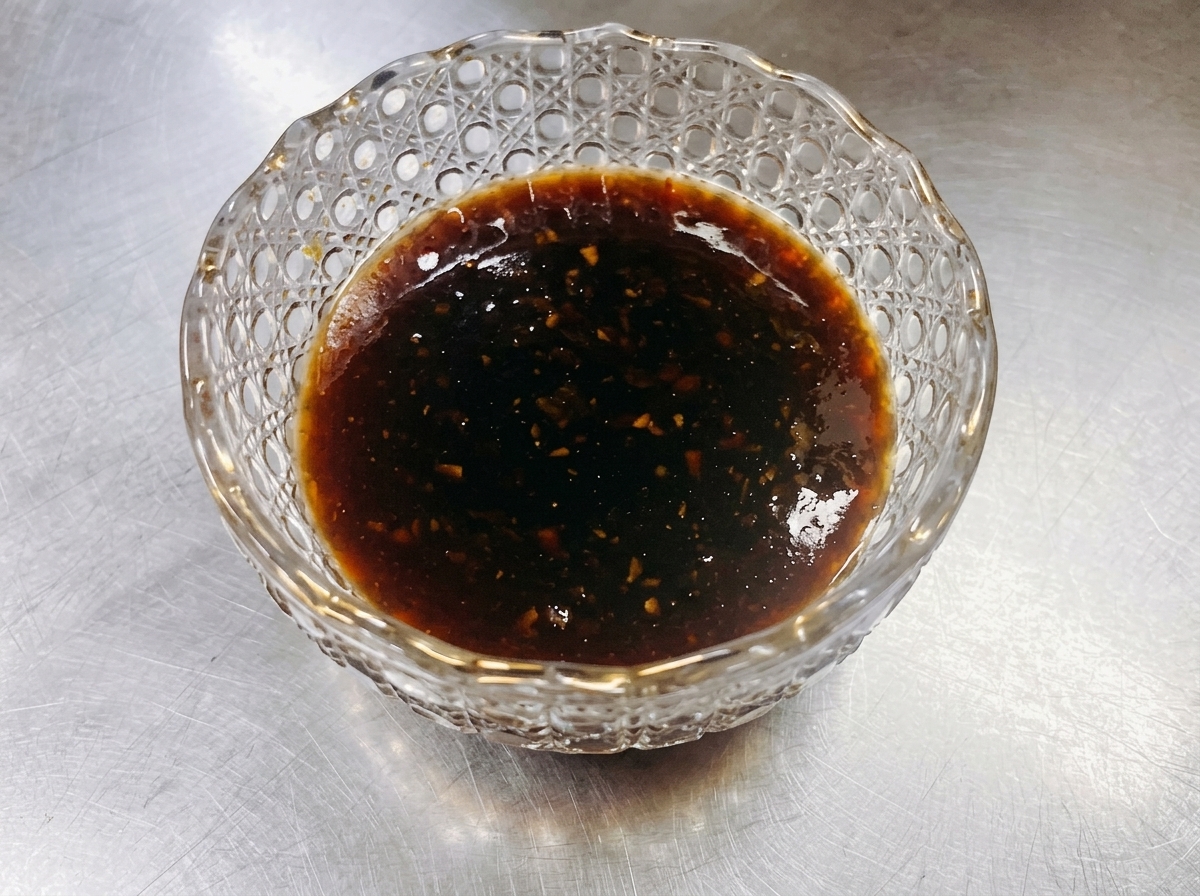 Rindfleischscheiben schmoren in einer Pfanne, während eine dunkle, glänzende Teriyaki-Sauce darüber gegossen wird.