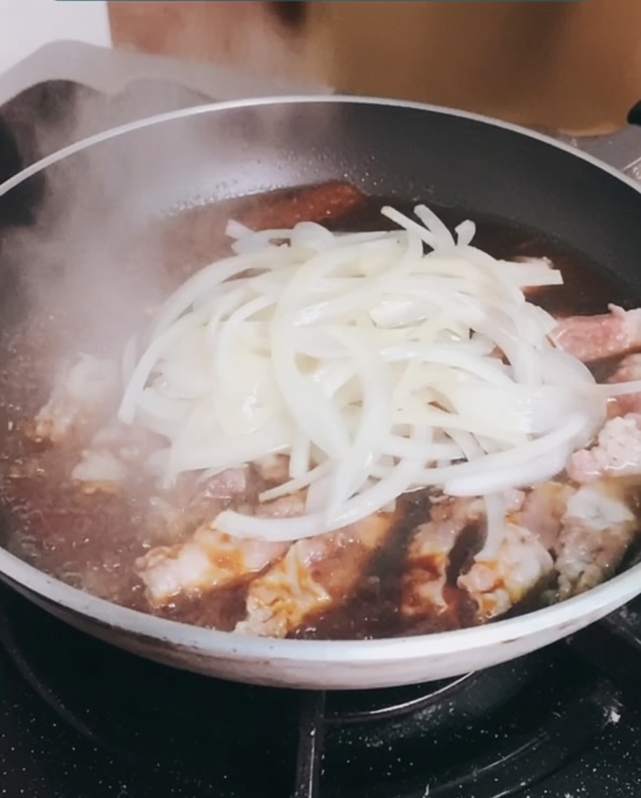 Die zuvor gebratenen Zwiebeln werden zurück in die Pfanne zum schmorenden Fleisch gegeben.