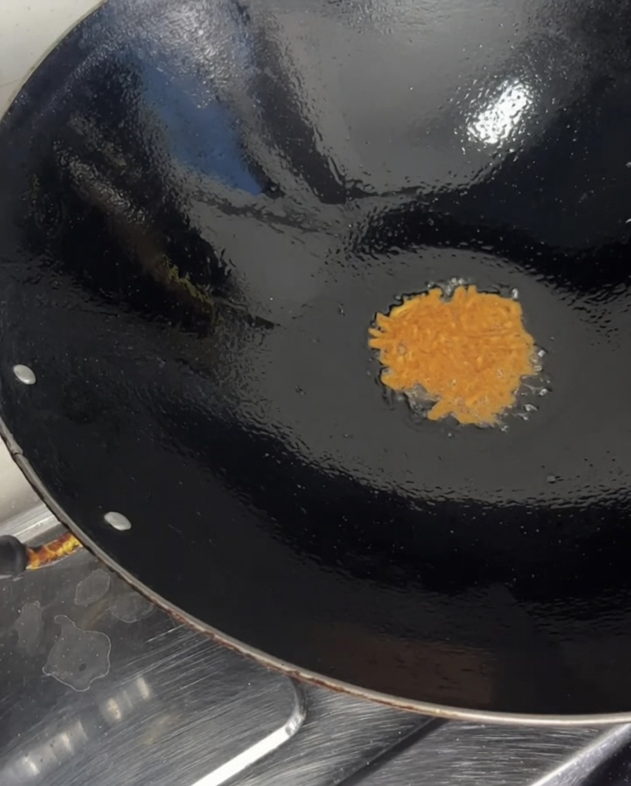 Leuchtend orangefarbener, roher Seeigelrogen wird aus einer durchsichtigen Schüssel in einen heißen Wok gegossen.