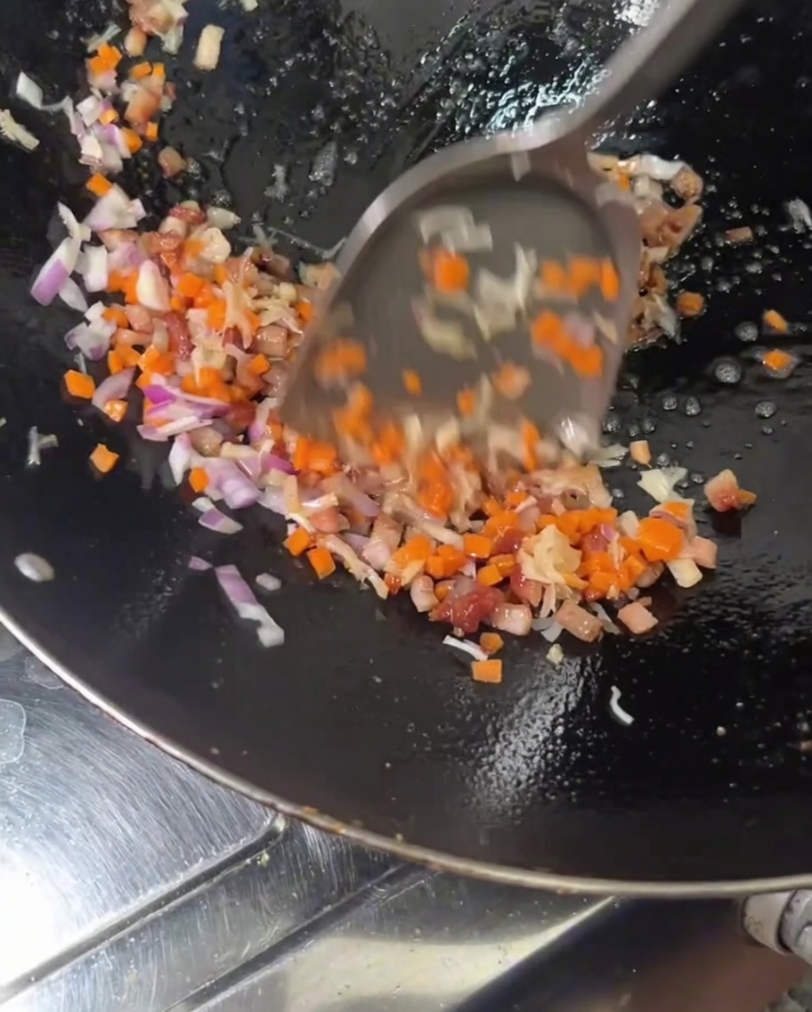 Gewürfelte orangefarbene Karotten und rote Zwiebeln werden zu gebratenem Fleisch und Jakobsmuscheln in einen heißen Wok gegeben.