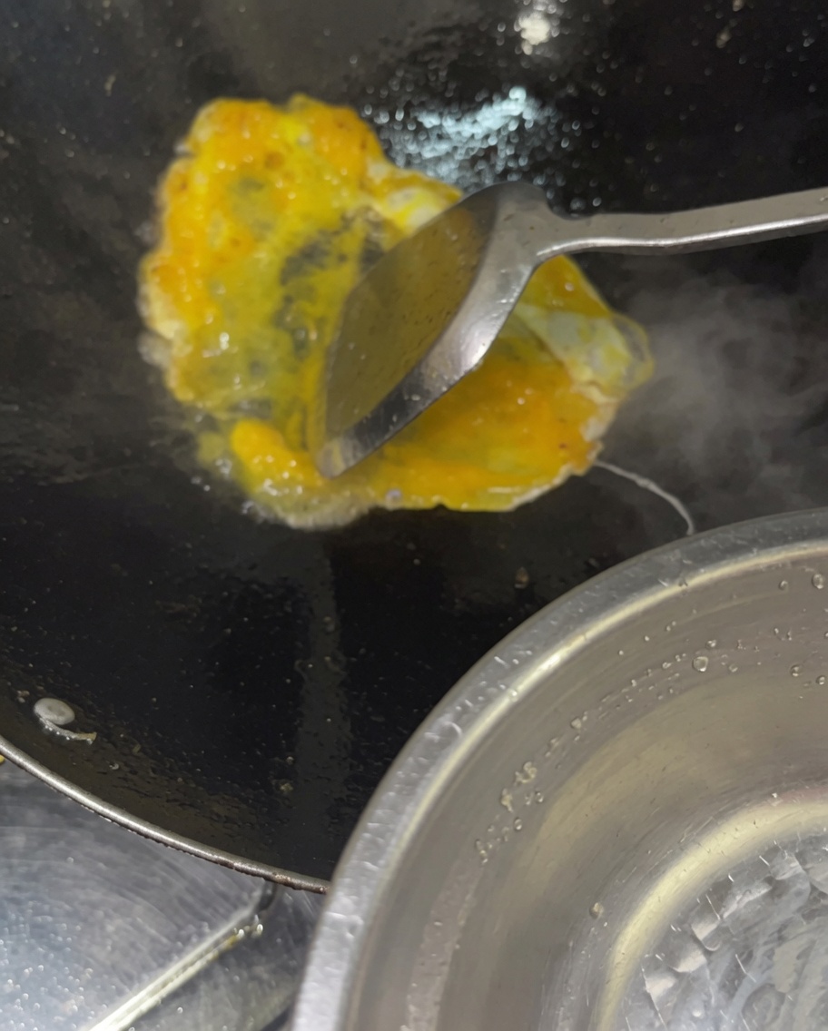 Ein Strahl verquirlter roher Eier wird in einen heißen Wok mit gekochtem Gemüse und Fleisch gegossen.