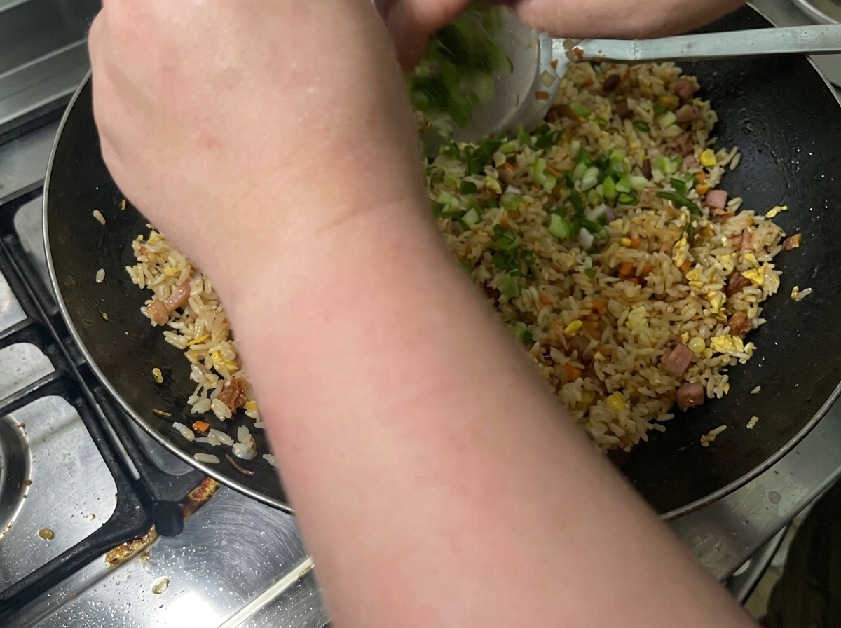 Gehackte Frühlingszwiebeln werden in einen Wok mit gewürztem gebratenem Reis geworfen.