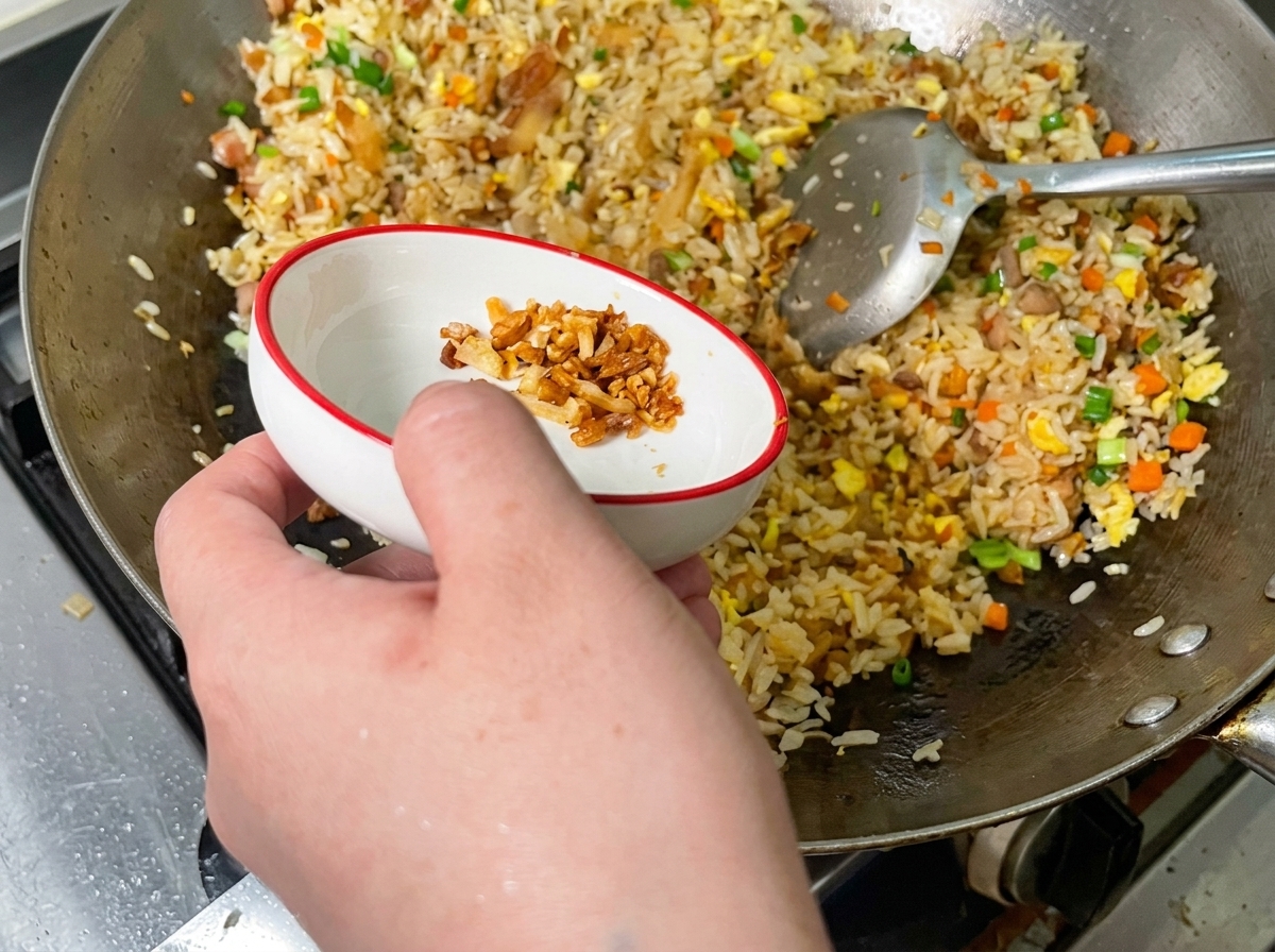 Knusprige goldene Schweinekrusten werden über eine bunte Portion gebratenen Reis in einem Wok gestreut.