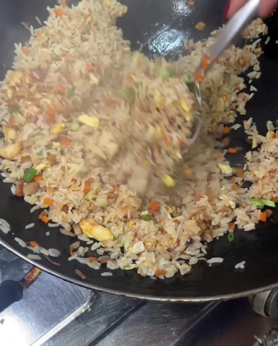 Gebratener Reis wird hoch in einem Wok geschwenkt und gemischt, um alle Zutaten gründlich zu verbinden.