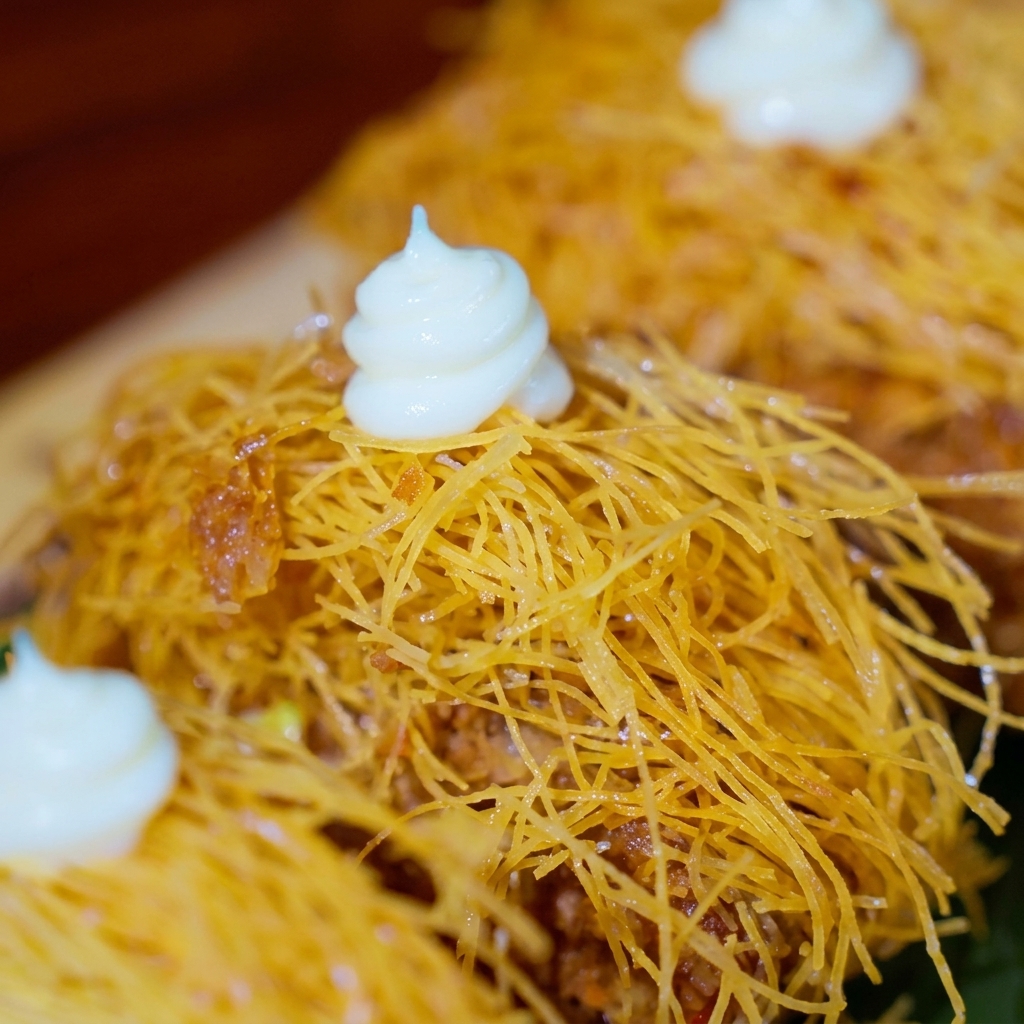 Knusprige, goldbraune Rindfleischpasteten mit weißen Saucen-Tupfen, verziert mit kleinen essbaren Blüten und winzigen roten Tomatenspalten.