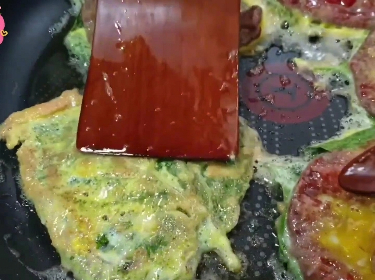 Ein Holzpfannenwender wendet einen goldbraunen Rindfleisch-Pfannkuchen in einer heißen Bratpfanne.