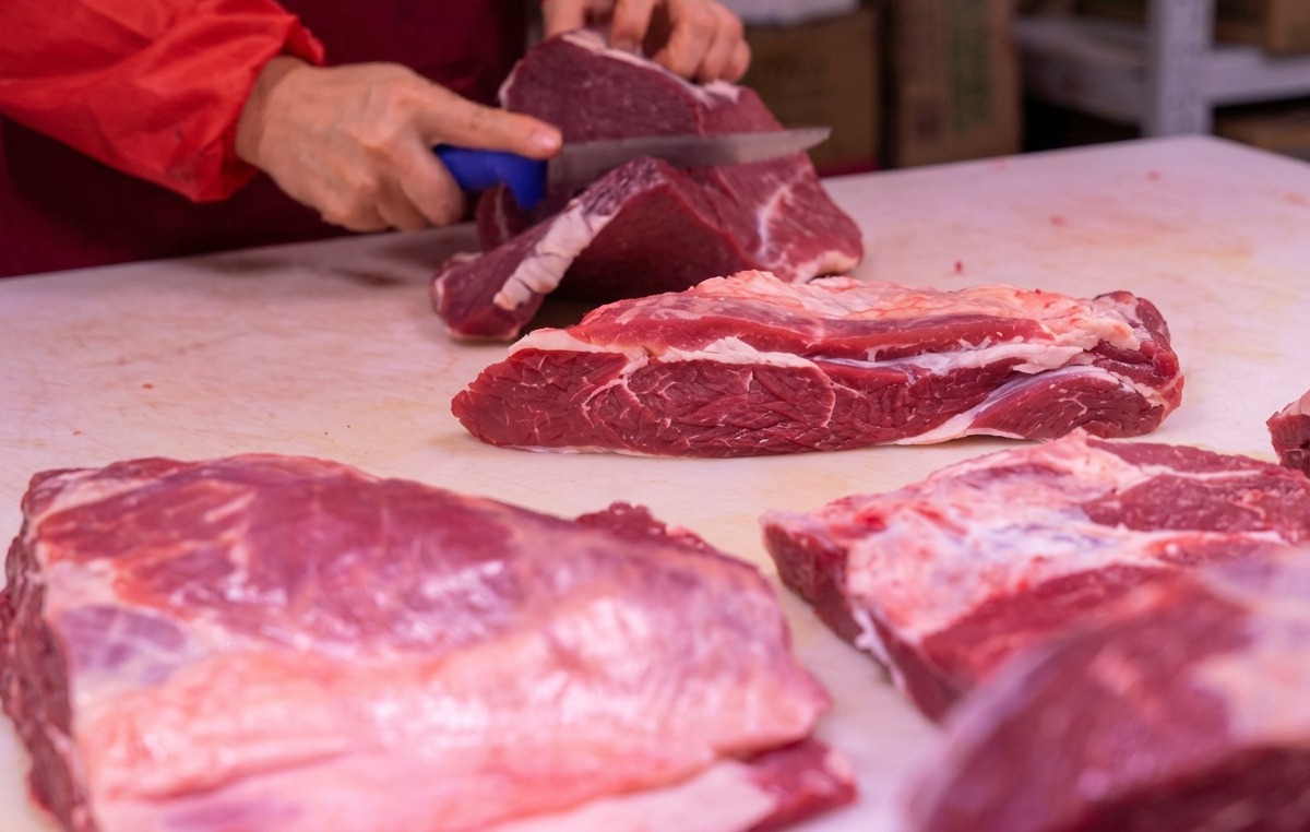 Hände, die mit einem scharfen Messer rotes Fleisch auf einem weißen Schneidebrett in Scheiben schneiden.