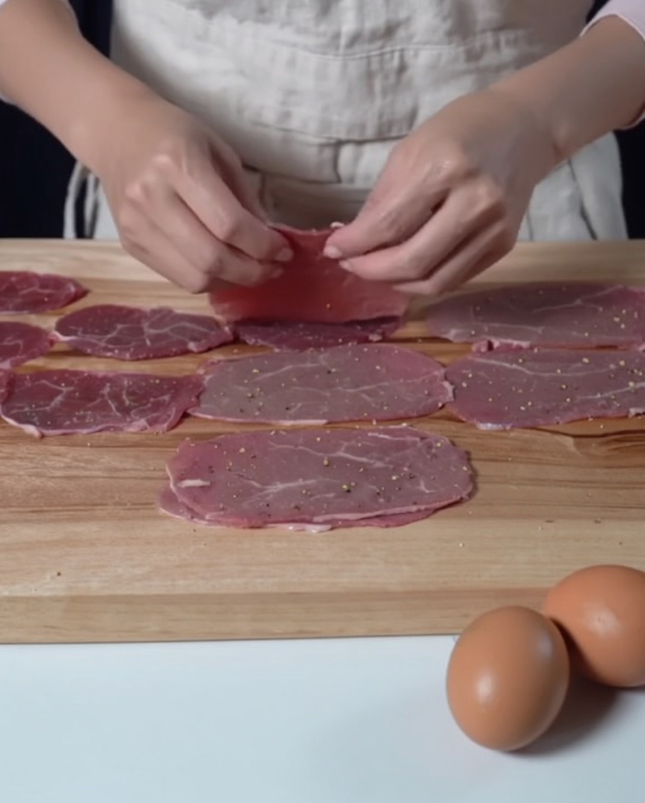 Gewürzte, dünne Rindfleischscheiben auf einem Holzbrett, bereit für das Mehlieren.