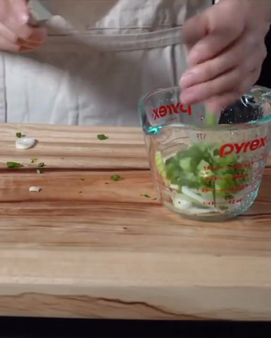 Gehackte Frühlingszwiebeln und Zwiebeln in einer Glas-Messkanne mit einer dunklen Sauce verrührt.