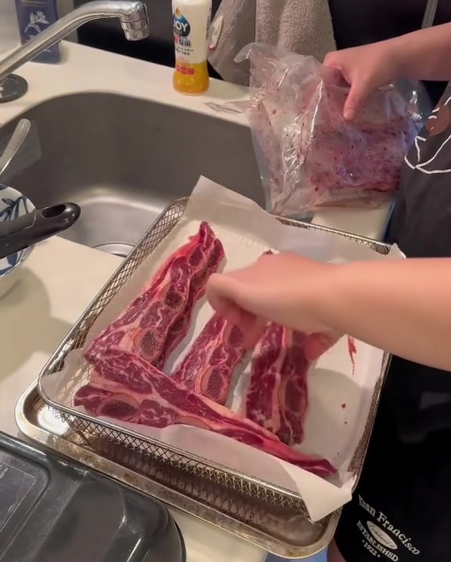 Rohe Rinder-Short-Ribs im Korb einer Heißluftfritteuse, bereit für den Garvorgang.
