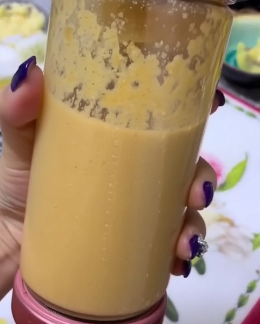 Eine Hand hält einen Mixerbecher mit einem glatten Frucht-Gemüse-Püree.