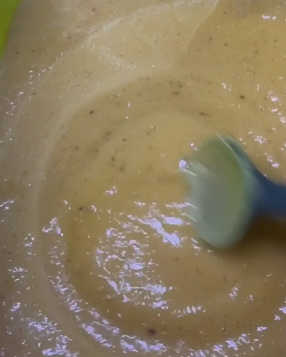 Eine gelblich-braune Marinade in einer hellgrünen Schüssel umrühren.