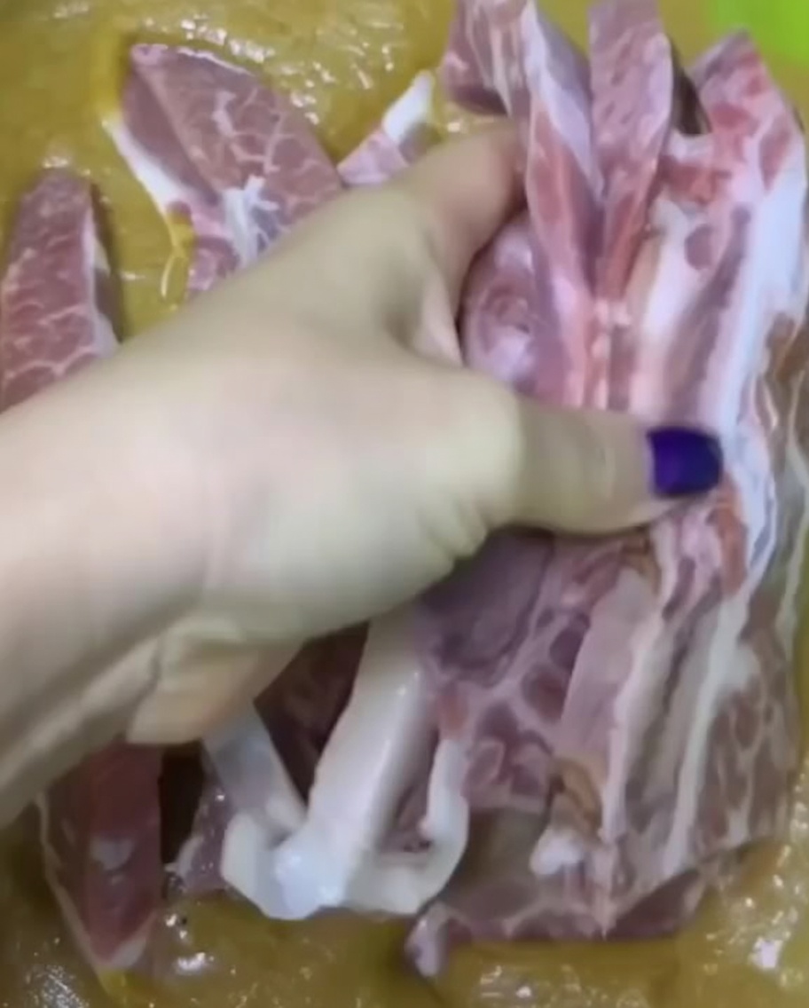 Ein Hand massiert rohe Rinderrippchen mit einer dickflüssigen Marinade.