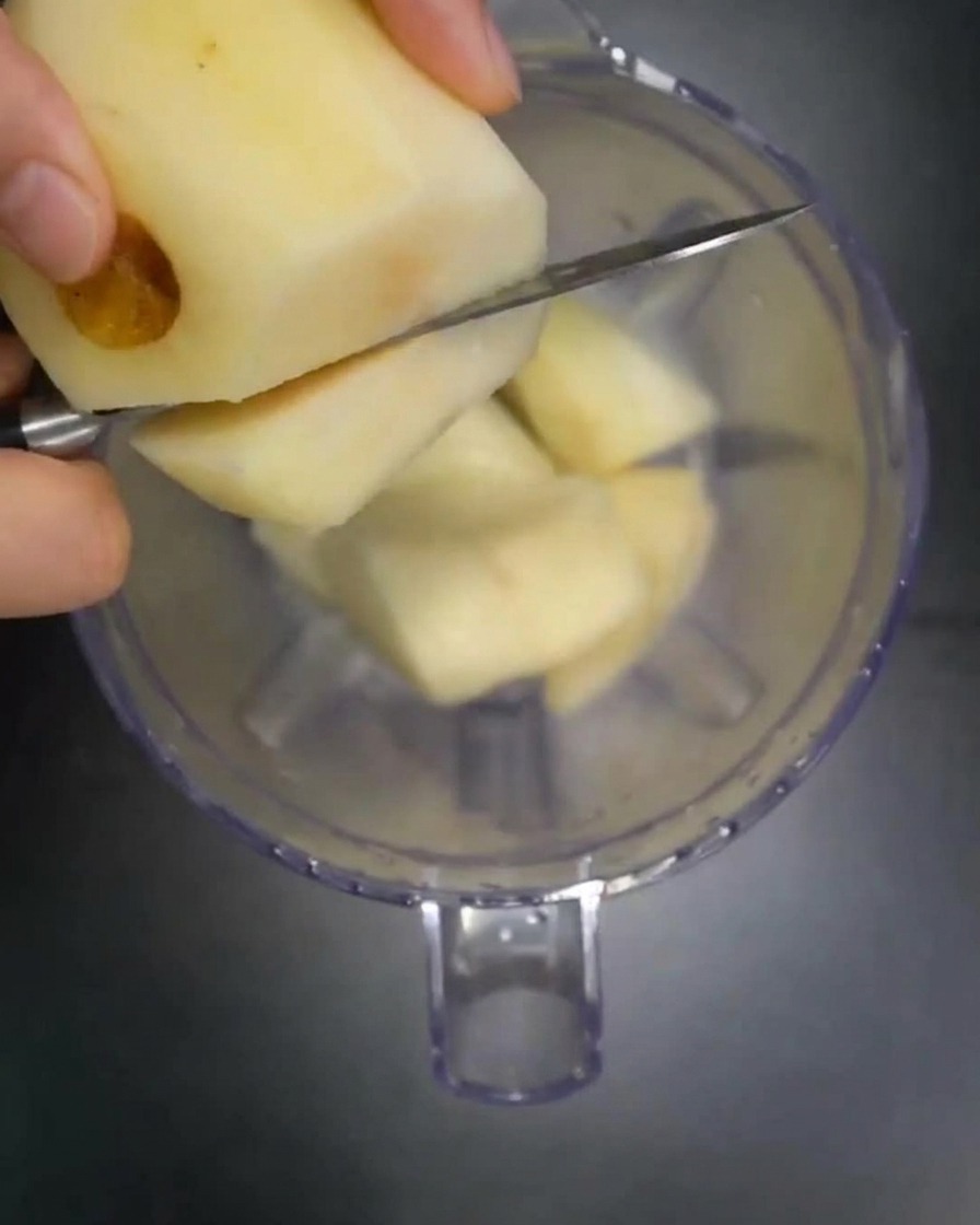 Stücke von frischer Birne, Apfel und Zwiebel, die in einen Standmixer gegeben werden.