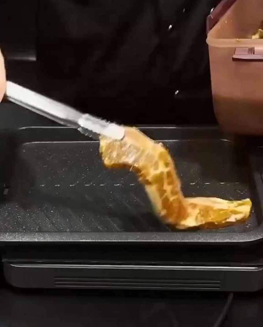 Marinierte Rippchen werden mit einer Grillzange auf eine heiße, rechteckige Grillpfanne gelegt.