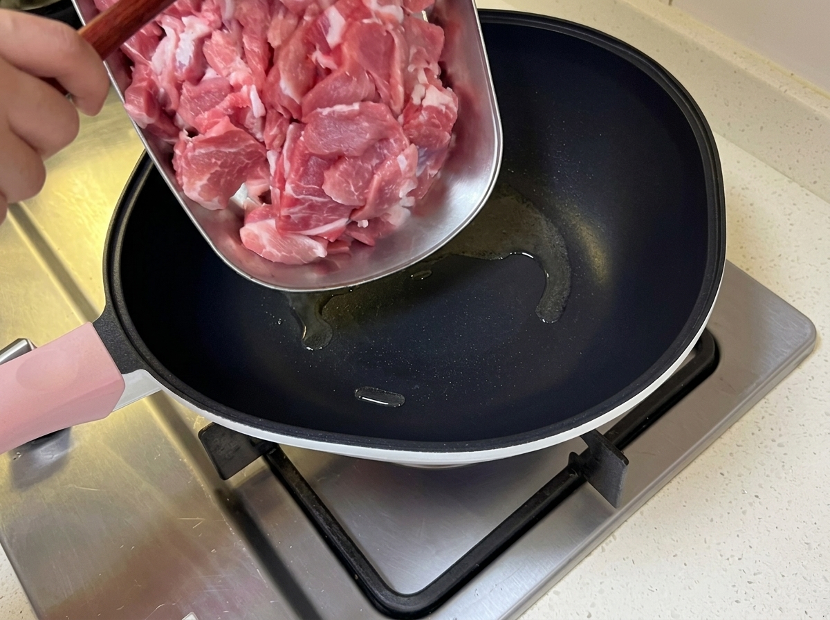 Dünn geschnittenes Schweinefleisch wird in eine heiße Pfanne mit schimmerndem Öl gegeben.