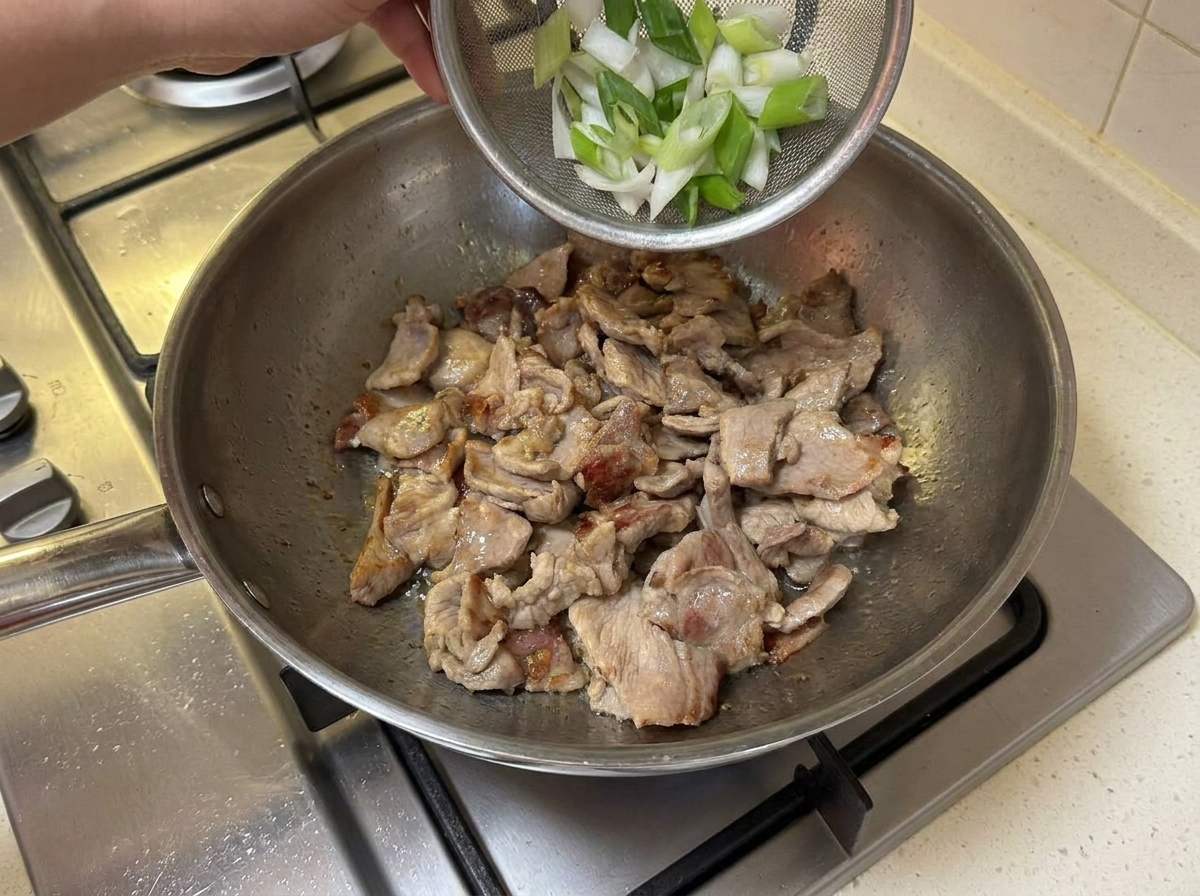 In Ringe geschnittene Frühlingszwiebeln werden zum angebratenen Fleisch in die Pfanne gegeben.