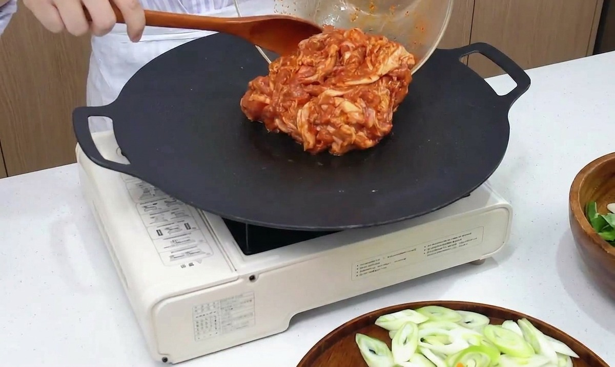 Marinierter scharfer Schweinebauch wird aus einer Glasschüssel auf eine heiße Grillpfanne gegeben.