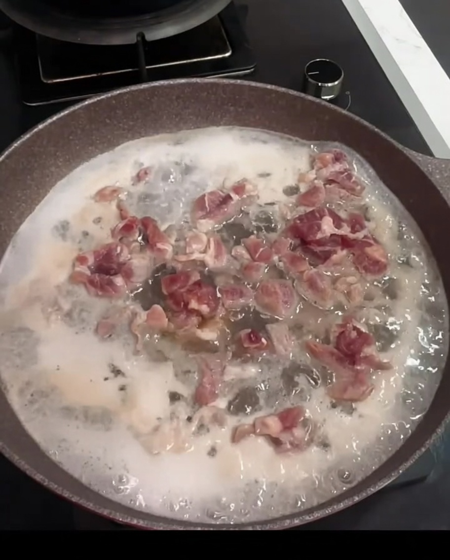 Schweinefleischstücke kochen in einem Topf mit Wasser, Kochwein und einem Lorbeerblatt.