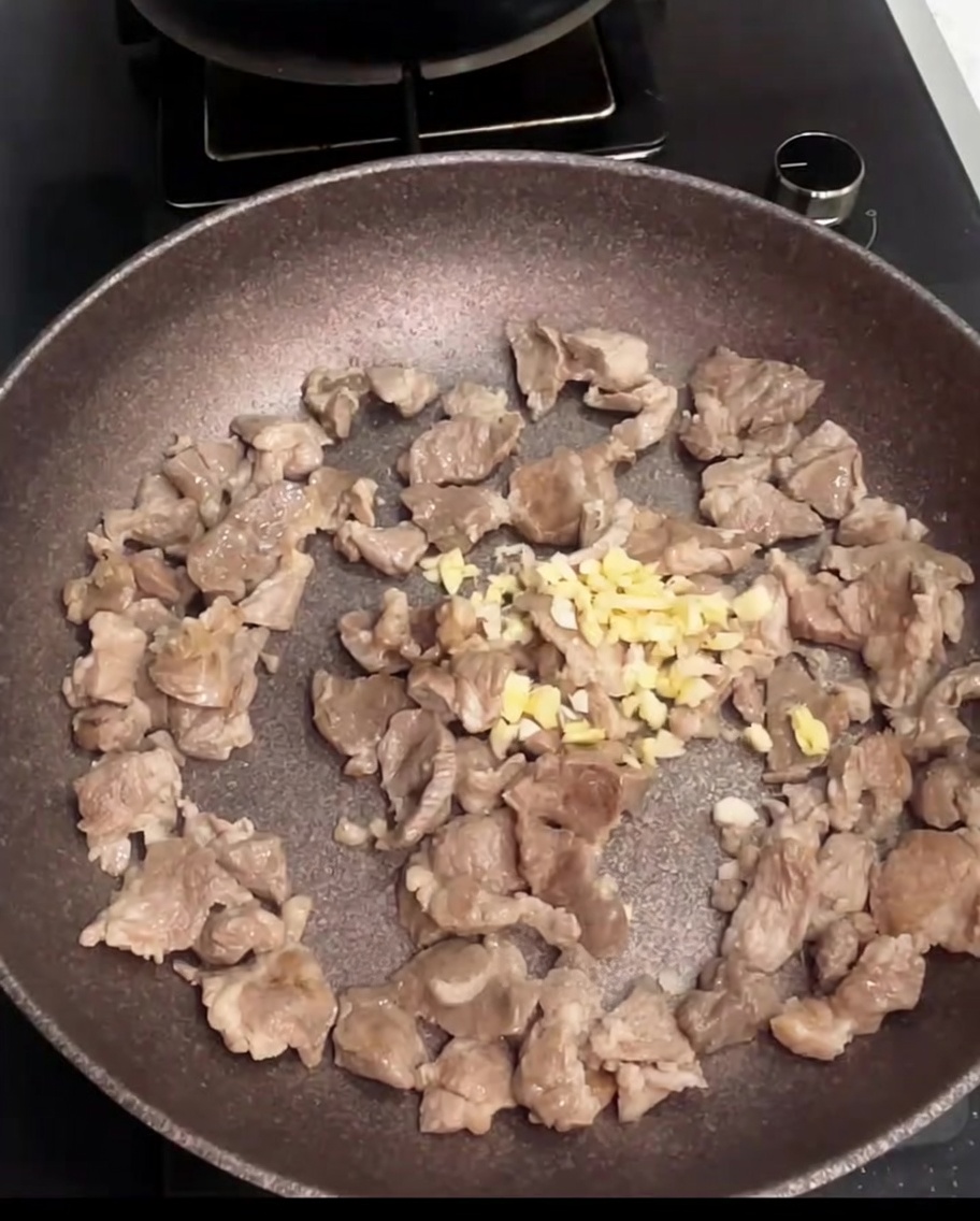Schweinefleischstücke werden in einer Pfanne mit frisch hinzugefügtem gehacktem Knoblauch angebraten.