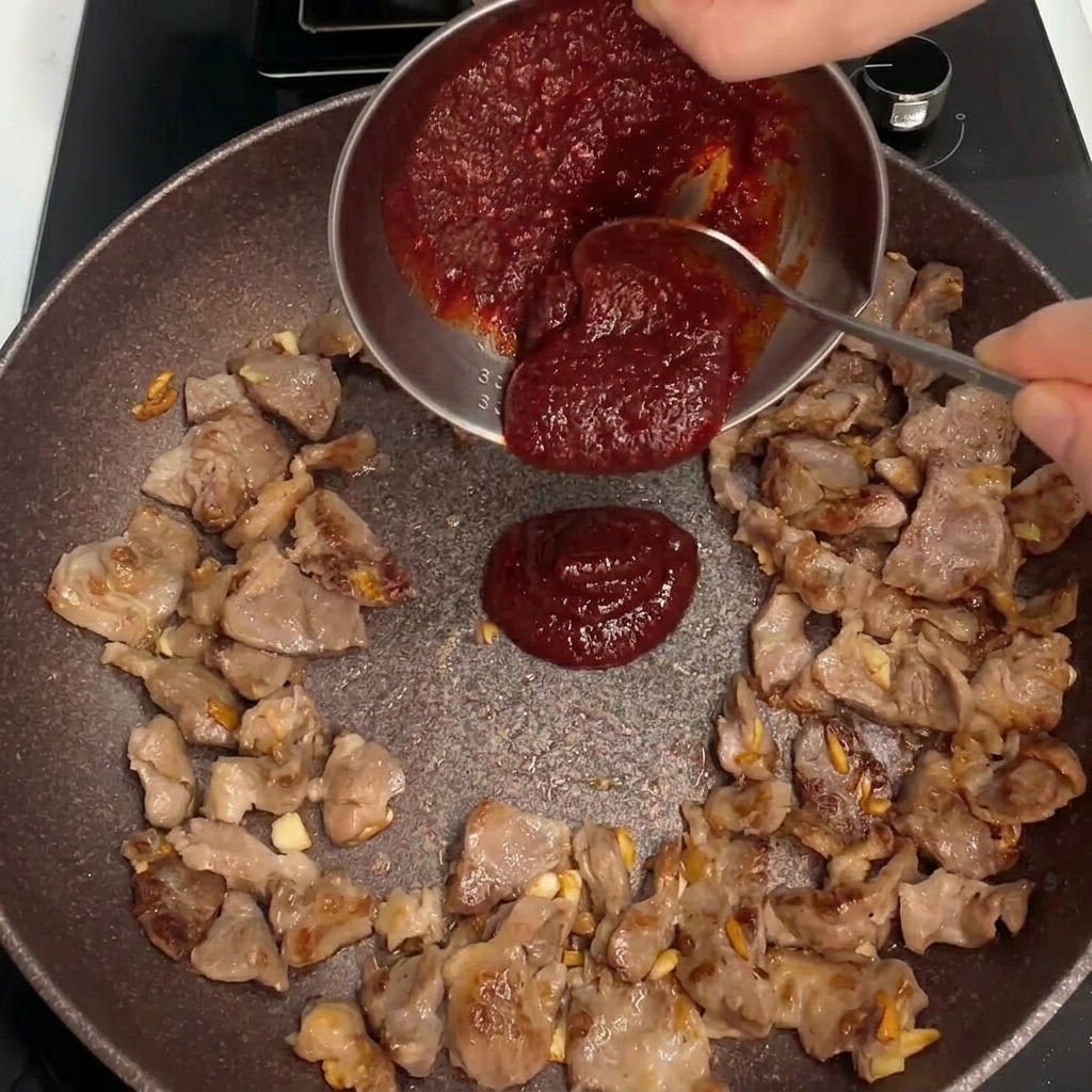Dicke rote Sauce wird in die Mitte der Pfanne mit dem angebratenen Schweinefleisch gegossen.