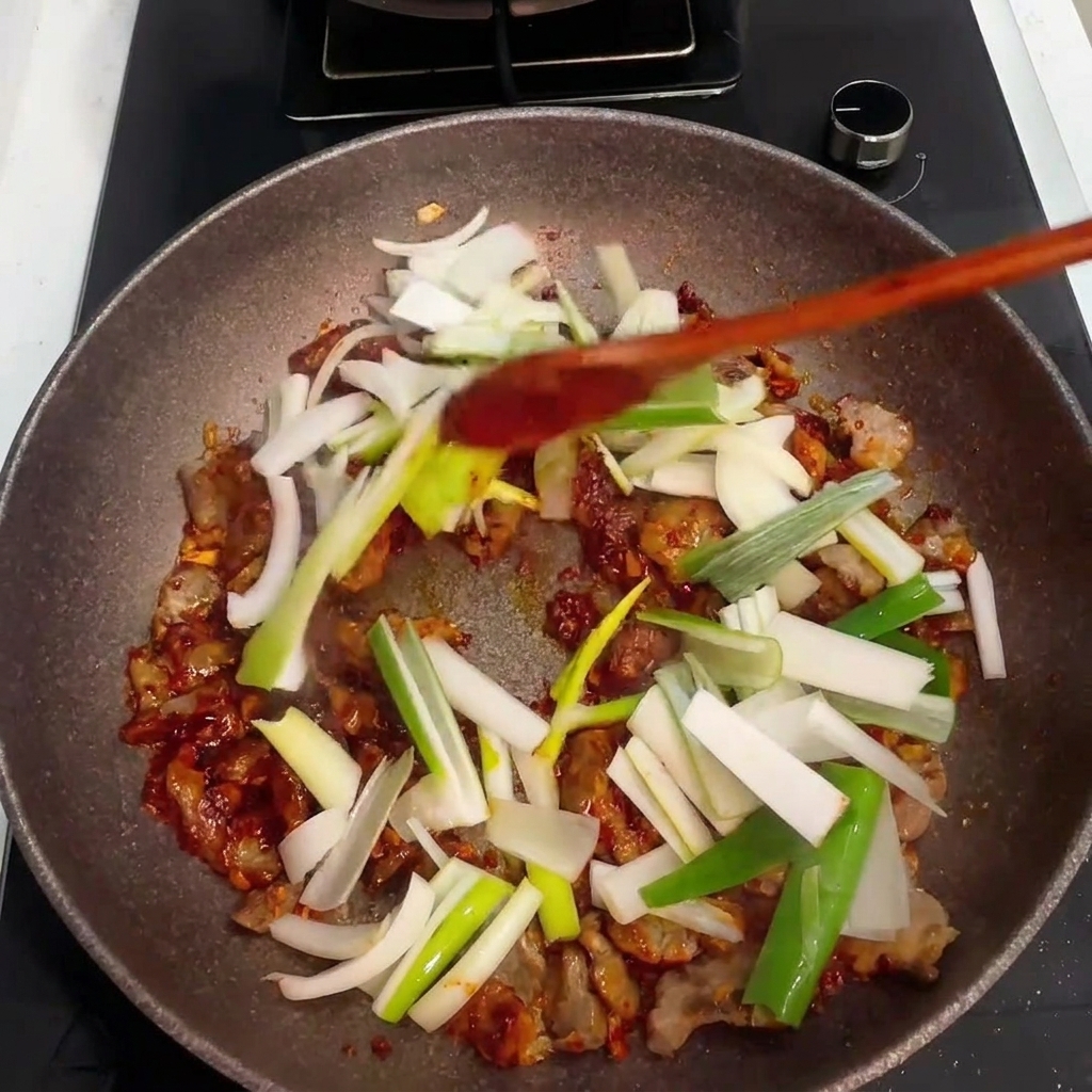 Frisch gehackte Zwiebeln und Frühlingszwiebeln werden in die Pfanne zu Schweinefleisch und Sauce gegeben.