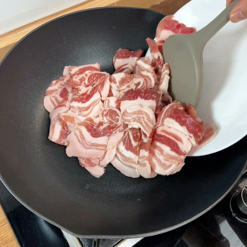 Rohe Schweinebauchscheiben in einer heißen Pfanne, der Bratprozess beginnt.