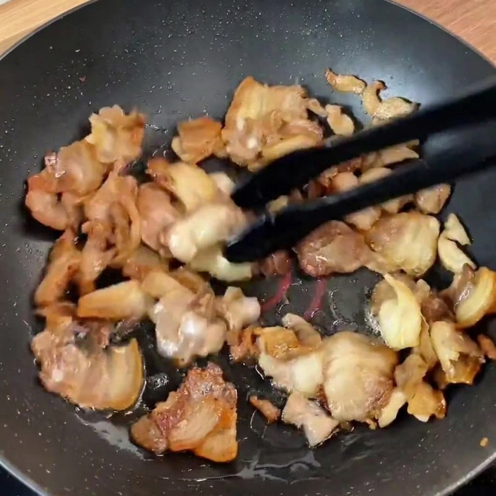 Frische grüne Paprikastreifen und rote Zwiebeln in der Pfanne mit dem angebratenen Schweinefleisch.