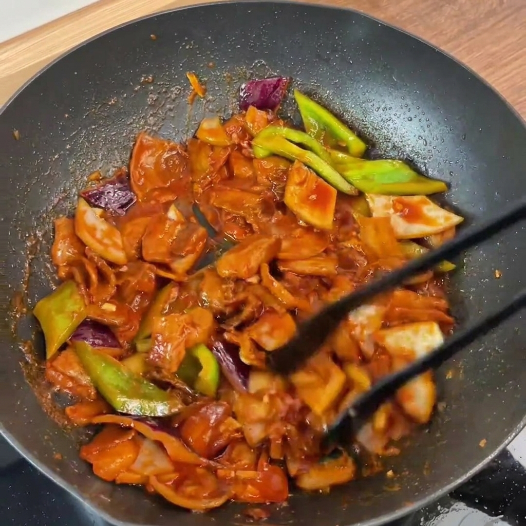 Das fertige Gericht wird mit einer Zange durchgemischt, alles ist glänzend mit der roten Sauce überzogen.