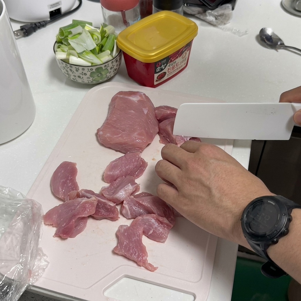 Eine Person schneidet rohes Schweinefleisch auf einem weißen Kunststoff-Schneidebrett mit einem Küchenmesser.