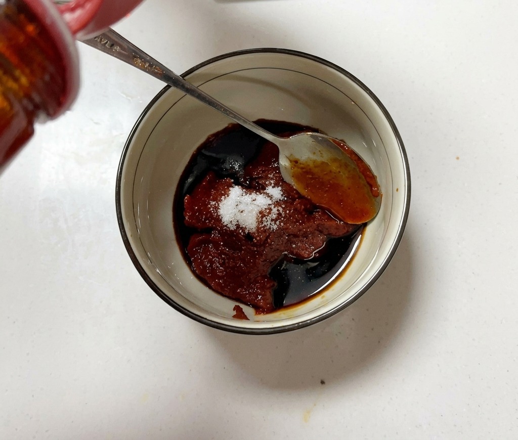 Eine kleine Schüssel mit Chilipaste, Zucker und Sojasauce wird mit einem Löffel vermengt.