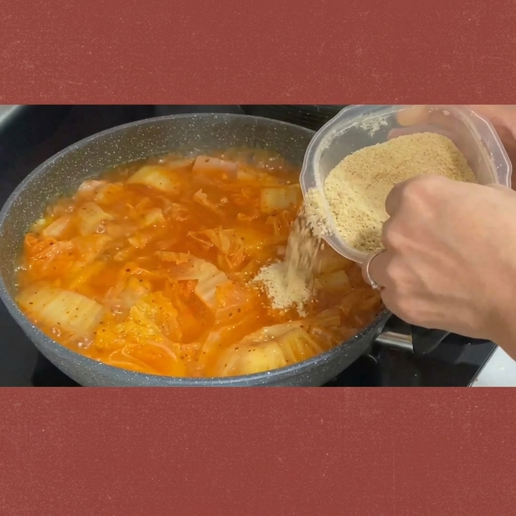 Zucker wird aus einem Behälter in den köchelnden Kimchi-Eintopf gestreut.
