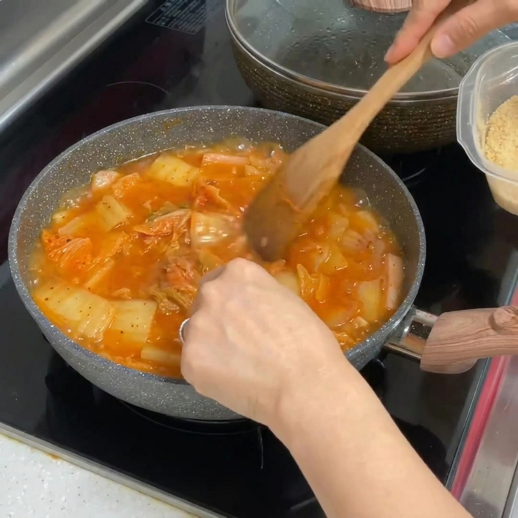 Gehackter Knoblauch wird in den kochenden roten Kimchi-Eintopf gerührt.