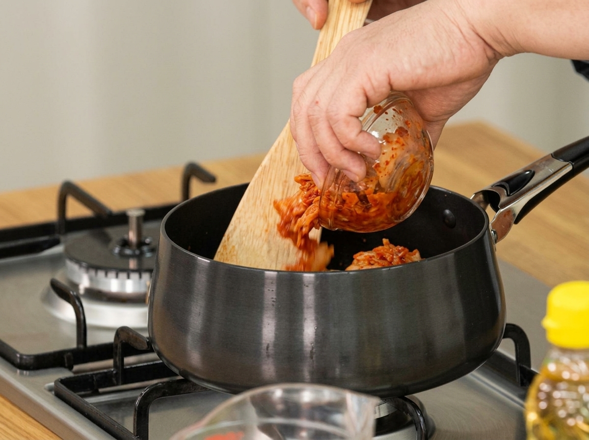 Gereiftes Kimchi wird mit einem Holzlöffel zum Anbraten in einen Topf gegeben.
