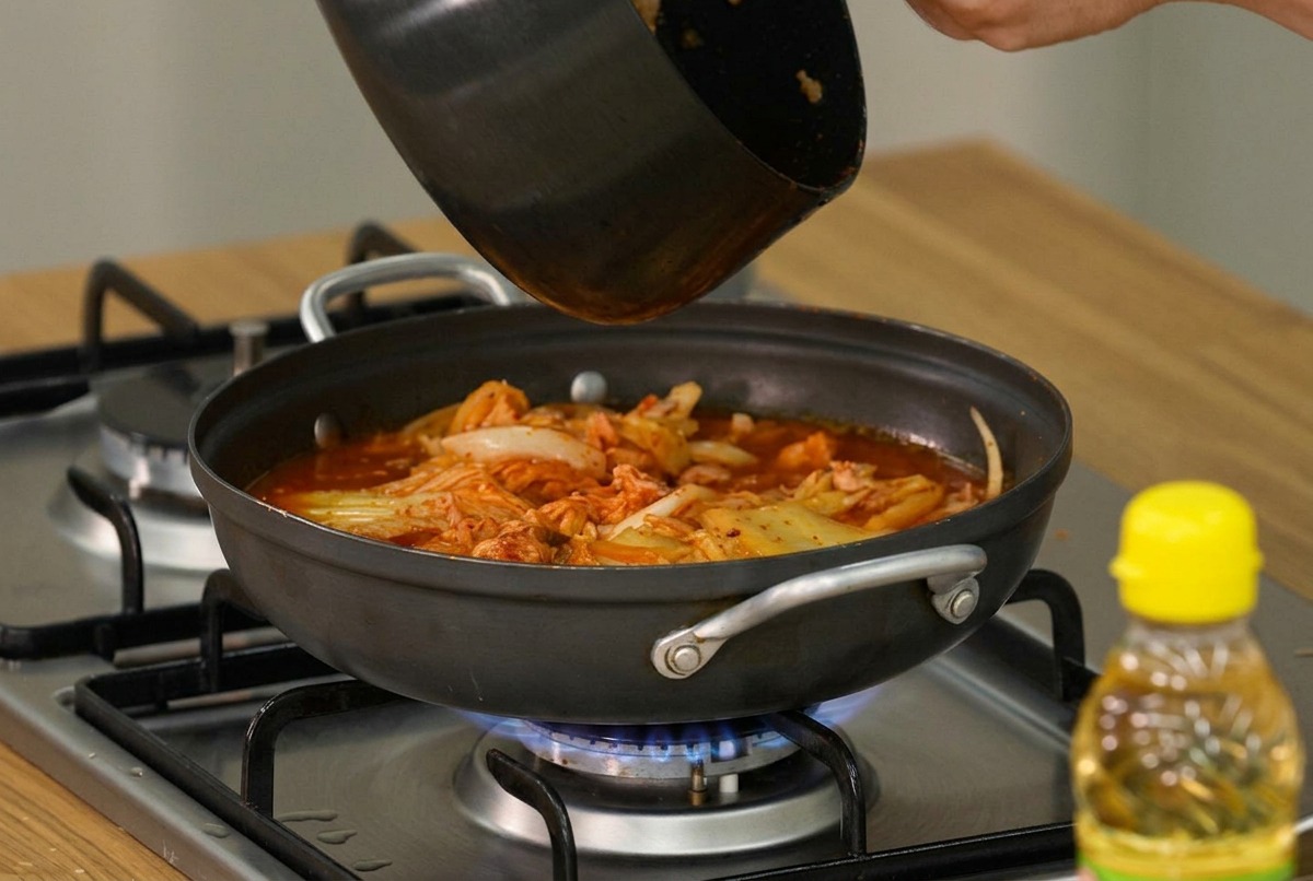Scheiben aus weichem Tofu und frische grüne Frühlingszwiebeln werden vorsichtig auf die Oberfläche des köchelnden Kimchi-Eintopfs gelegt.