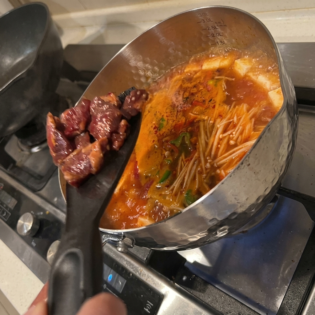 Marinierte Rindfleischstücke werden in den köchelnden Kimchi-Tofu-Eintopf gegeben.