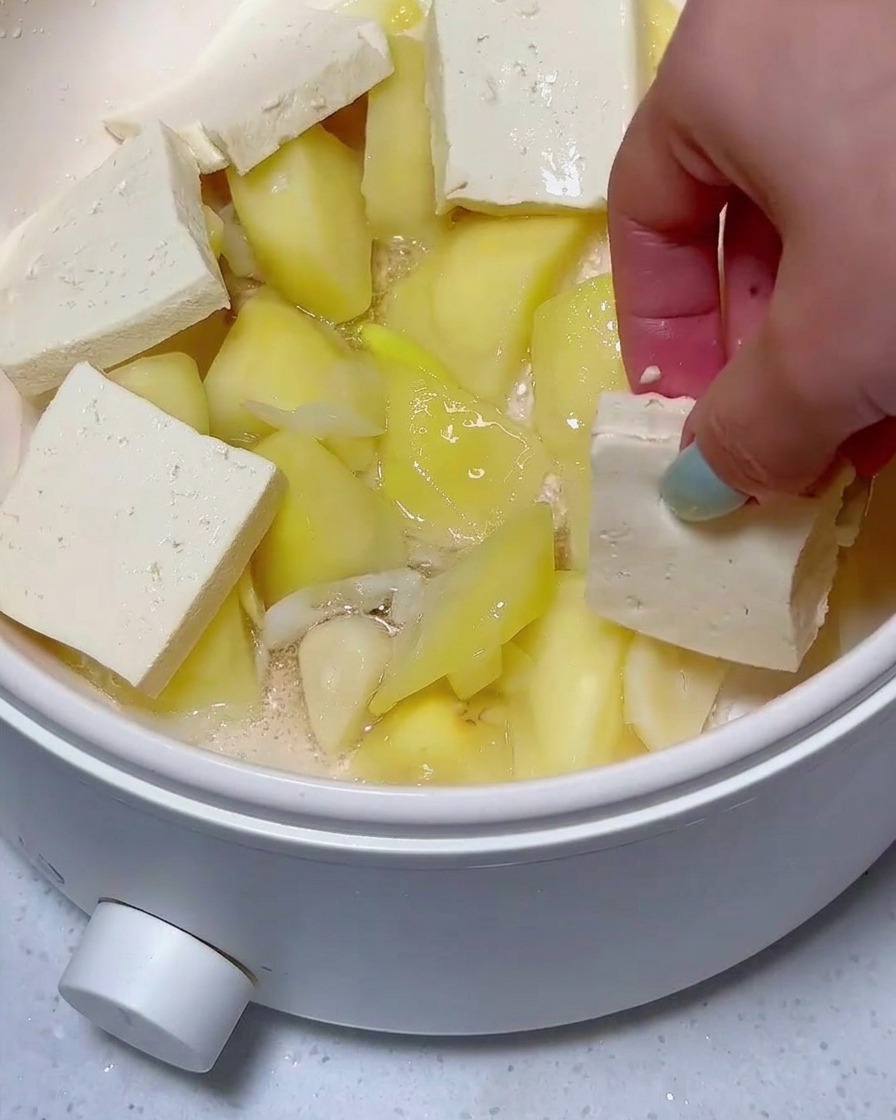 Geschichtete Tofu- und Frühstücksfleischscheiben liegen auf Kartoffelstücken in der Pfanne.