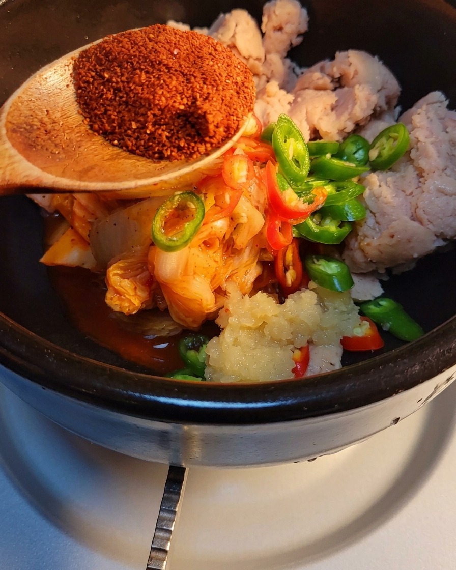 Koreanisches Chilipulver wird über die Zutaten im Steintopf gestreut.