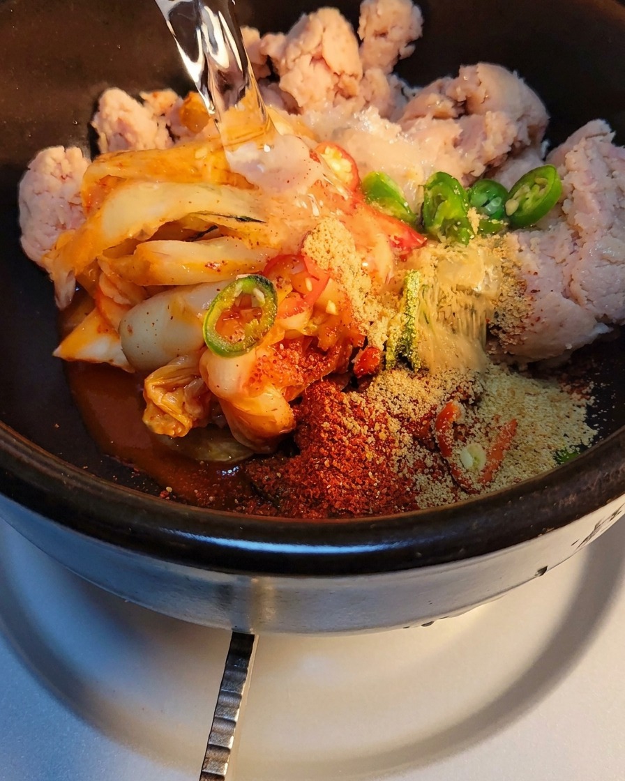 Wasser wird in den Steintopf mit Kimchi und Gewürzen gegossen, bereit zum Erhitzen.