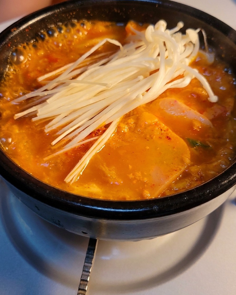 Ein Steintopf mit sprudelnder Kimchi-Suppe, belegt mit Enoki-Pilzen.