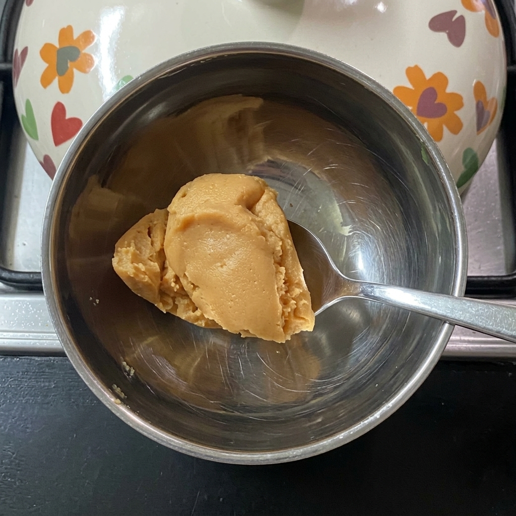Ein Löffel rührt Miso-Paste in warmem Wasser in einer kleinen Schale an.