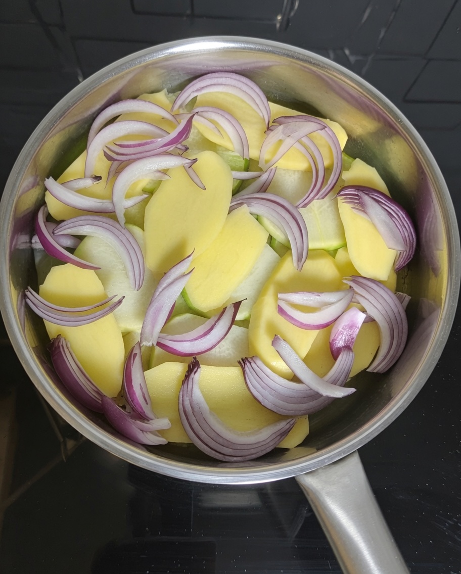 Stücke aus der Makrelendose werden auf die Kartoffel- und Zwiebelschicht im Topf gelegt.